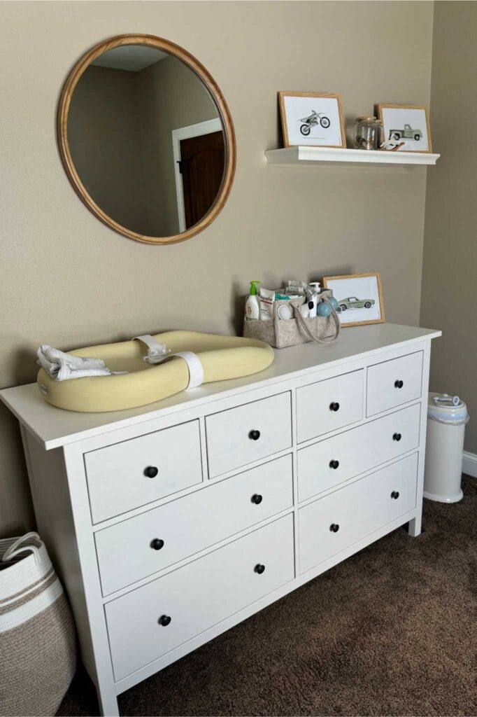 Nursery with a white dresser topped with a Keekaroo changing pad and diaper caddy, with a mirror hanging above.